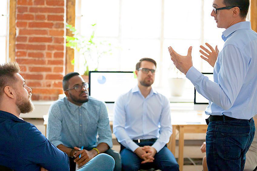 Confident male leader mentor coach speaking at diverse team meeting